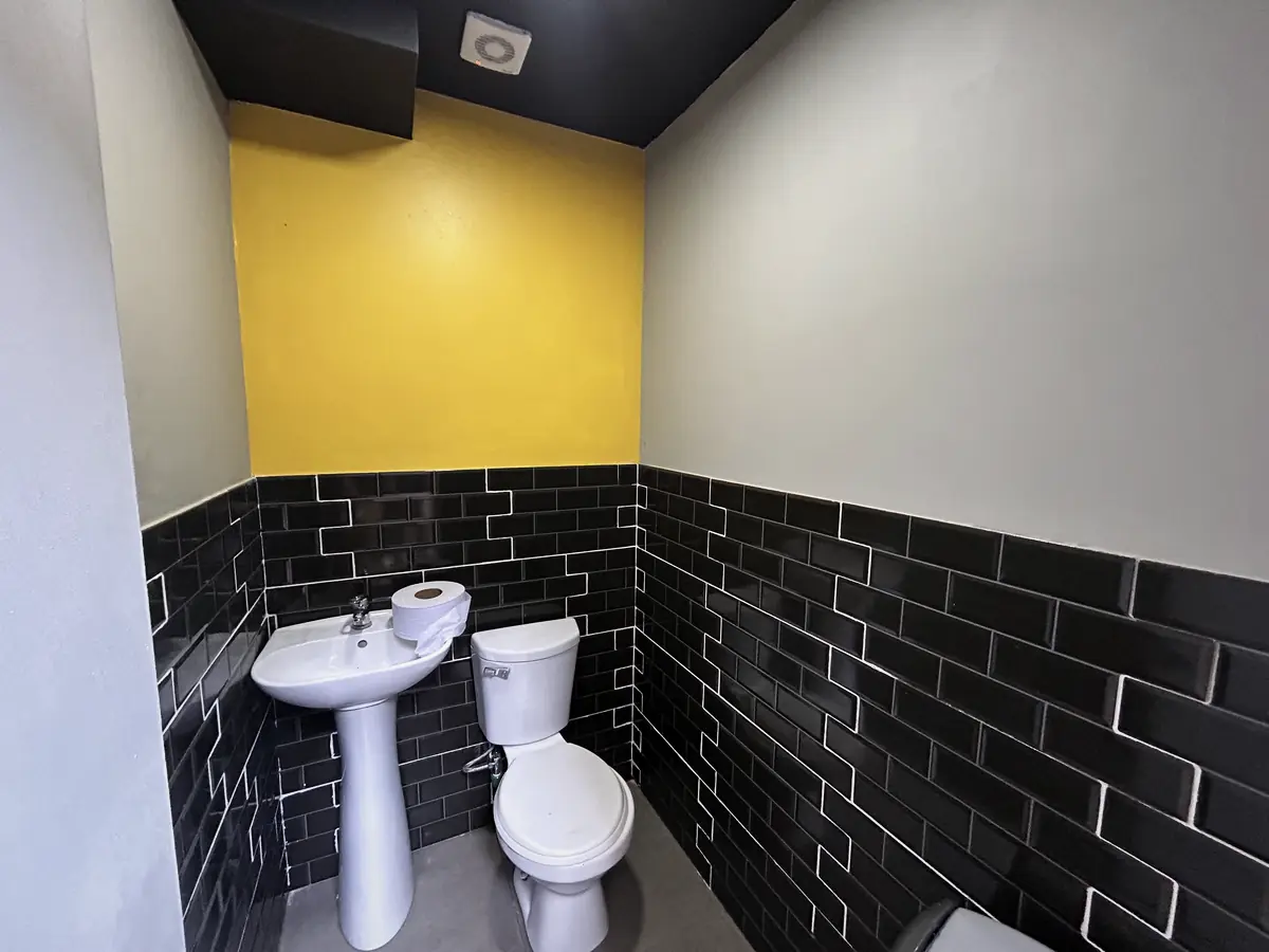Baño con cerámica negra y muro amarillo